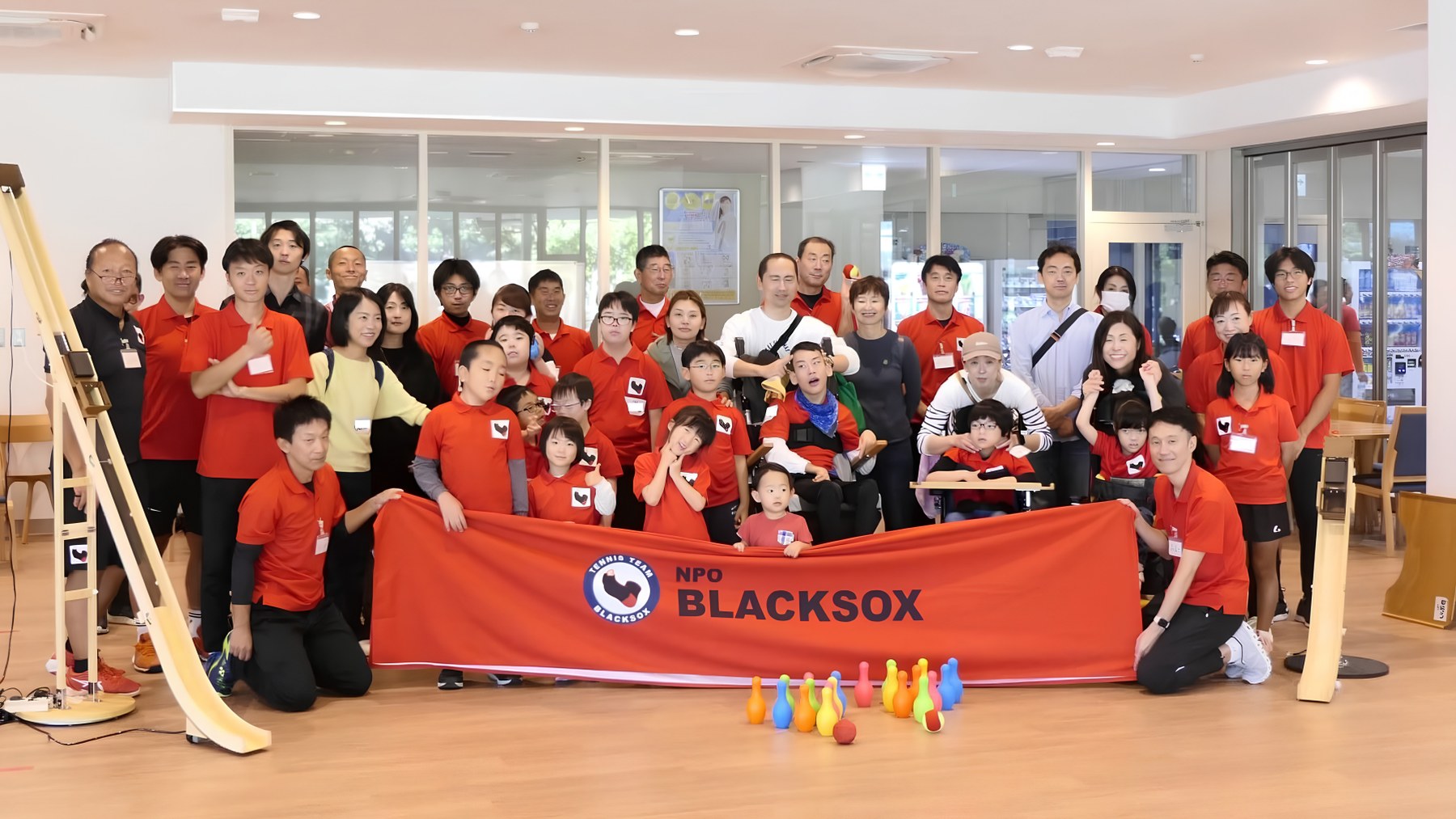 BLACKSOXの横断幕を囲んで、赤いシャツを着た子どもたち・保護者・スタッフが並んだ集合写真